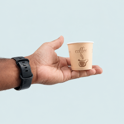 Hand holding a small paper cup with 'coffee' text on a light blue background